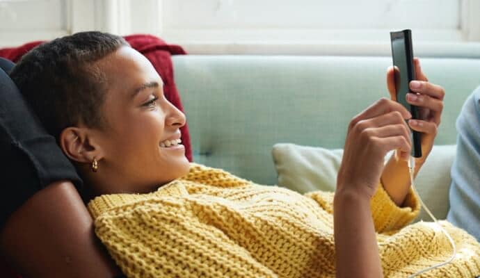 vrouw op bank die op mobiele telefoon kijkt en Norton 360 met AntiVirus Plus start.