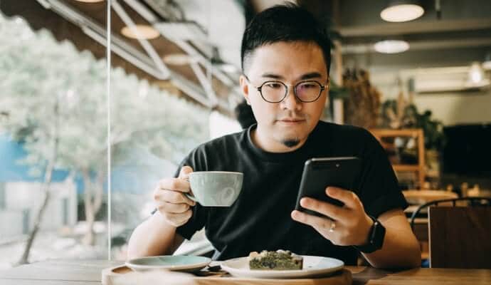 Man die van een koffie geniet en naar mobiele telefoon kijkt waarop Norton 360 Standard wordt gestart.